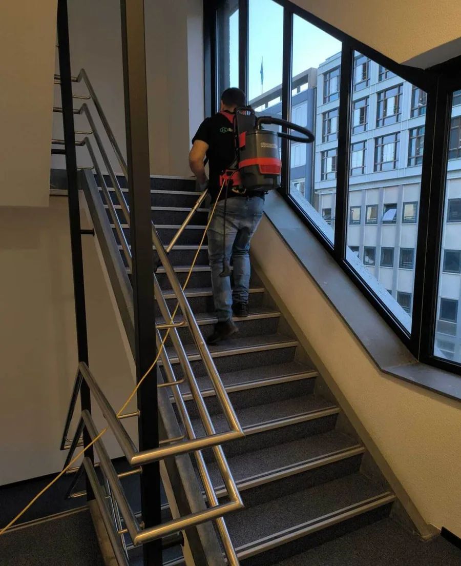 Radix-medewerker zuigt een trappenhuis met rugstofzuiger
